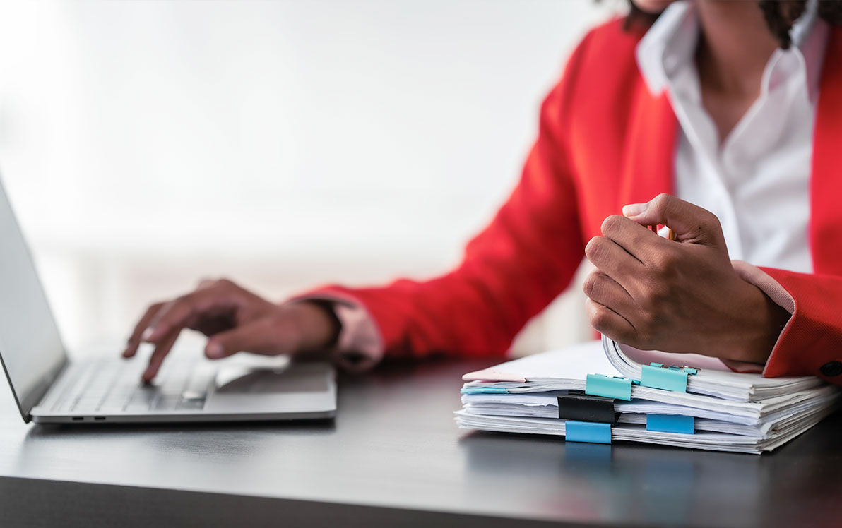 Study coordinator sorting through paperwork while typing on laptop