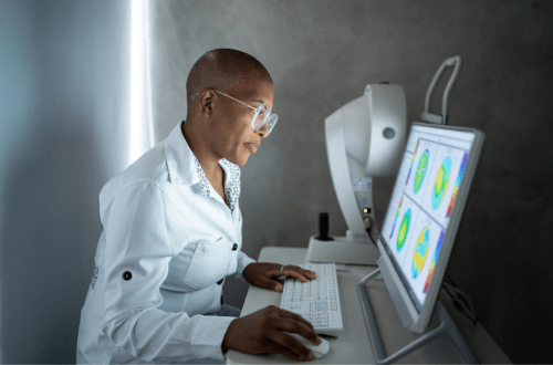 A woman in a lab coat working on a computer for ophthalmology research and ocular drug development