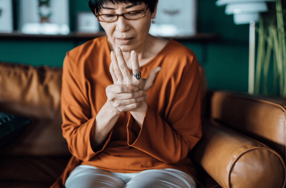 Older Asian woman in a Inflammatory Diseases clinical trial holds her hand as if in pain. Representing how CROs help patients with inflammatory diseases.