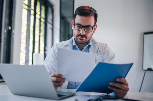 A male clinician looking at documents representing TMF services outsourced to CROs.
